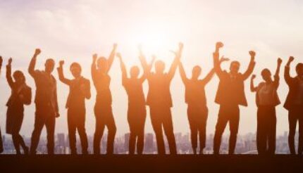 a team of people, mixed genders in silhouette with the sun behind them. All team members have their arms raised, indicating success and happiness