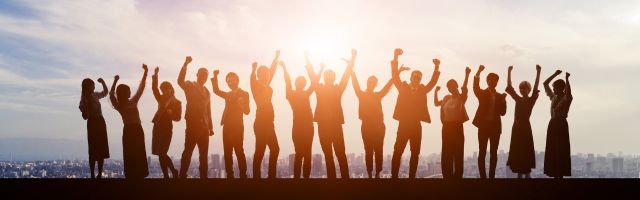 a team of people, mixed genders in silhouette with the sun behind them. All team members have their arms raised, indicating success and happiness