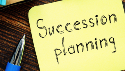 A yellow Post-It note on a wooden background with Succession planning written on it